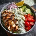 Homemade Greek Chicken Bowls filled with seasoned chicken, tomatoes, cucumbers, red onions, feta, lettuce, and tzatziki.