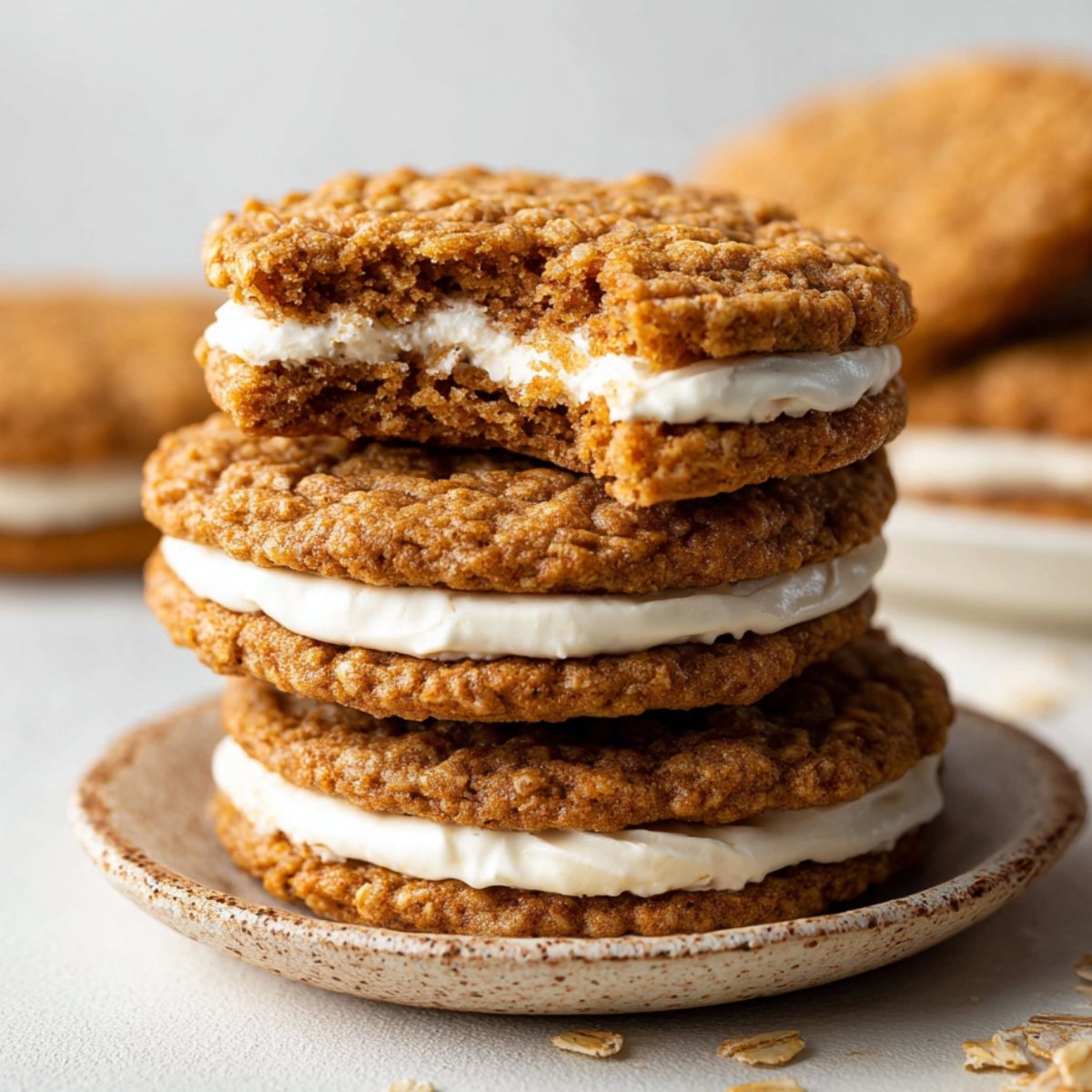 Homemade Oatmeal Cream Pies with one showing a bite taken out, revealing the creamy filling between the oatmeal cookies. The cookies are golden brown and placed on a simple ceramic plate.