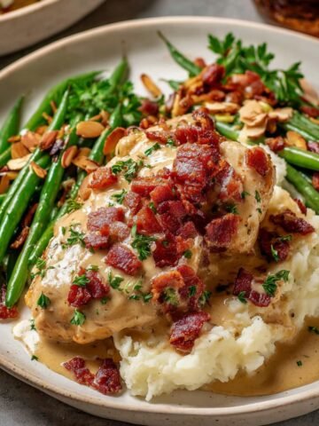 Smothered chicken with mashed potatoes, crispy bacon, parsley, and a side of green beans with toasted almonds.