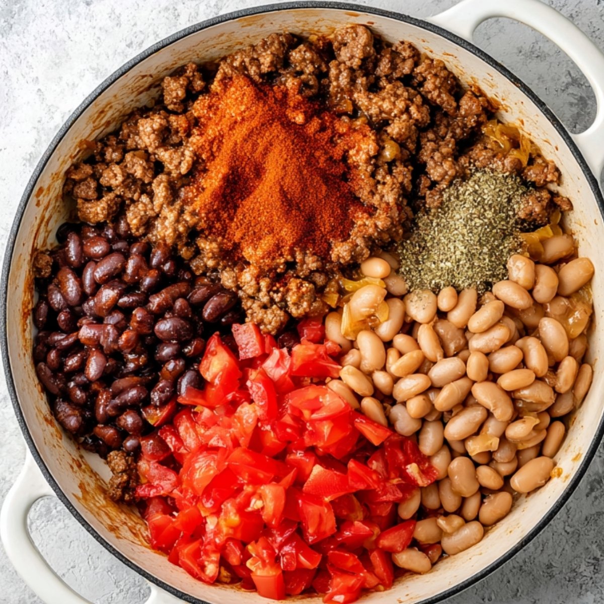 Skillet filled with cooked ground beef, black beans, pinto beans, diced tomatoes, and taco seasoning before stirring