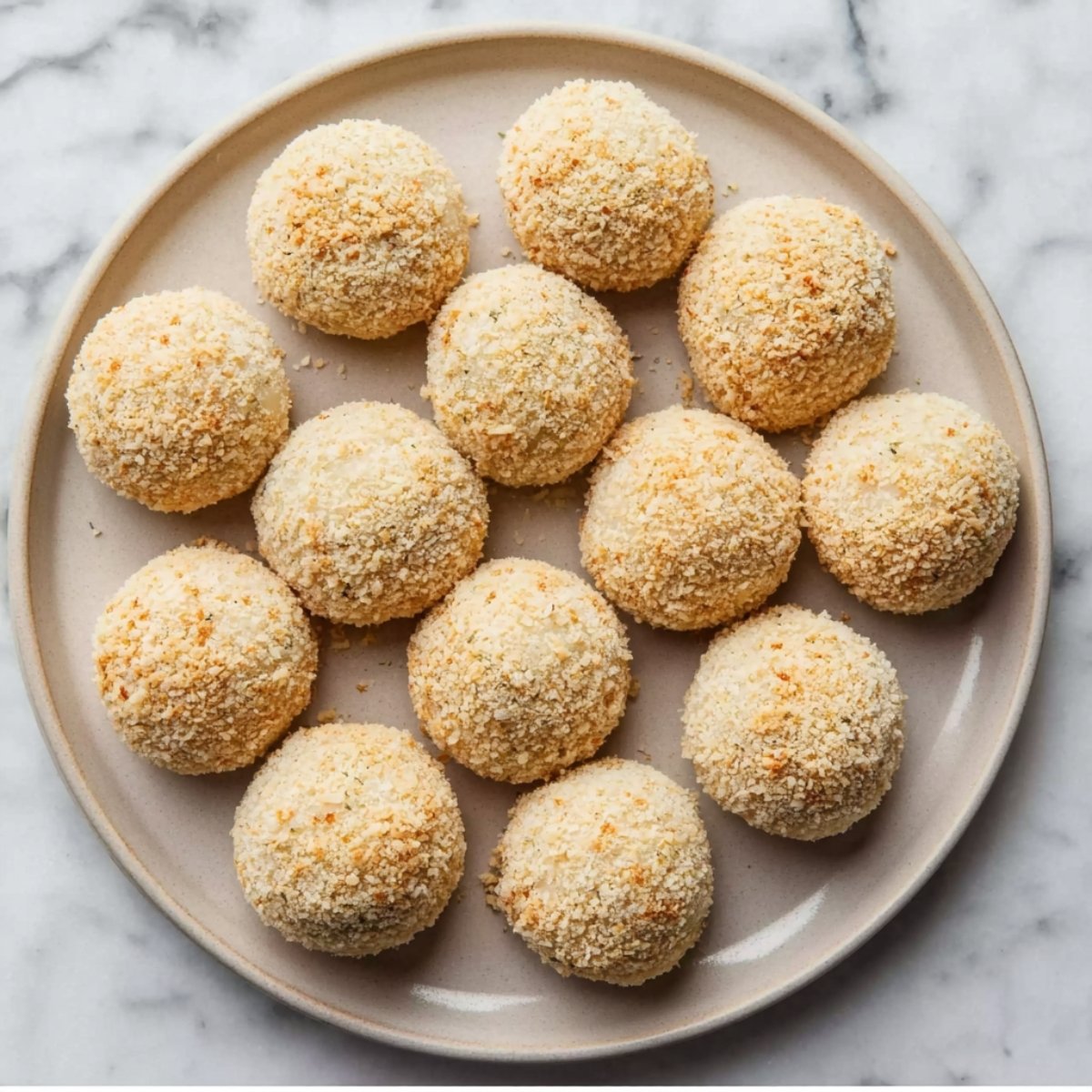 A plate of uncooked rice balls, coated in breadcrumbs, ready to be fried.