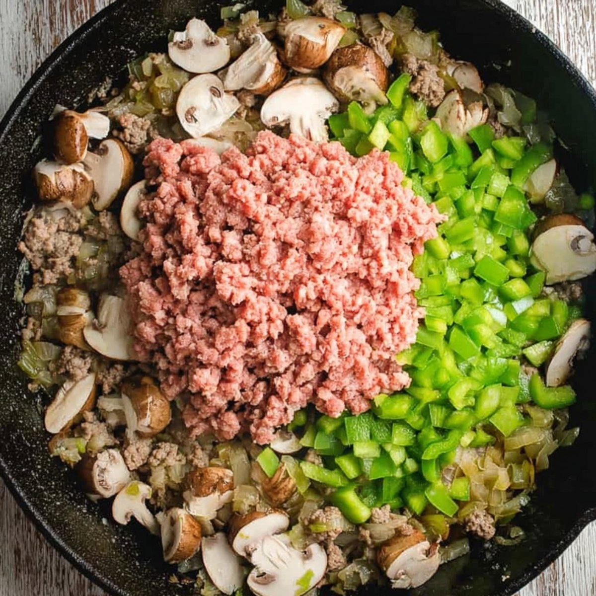 Ground beef being browned in a skillet with onions and green bell peppers.