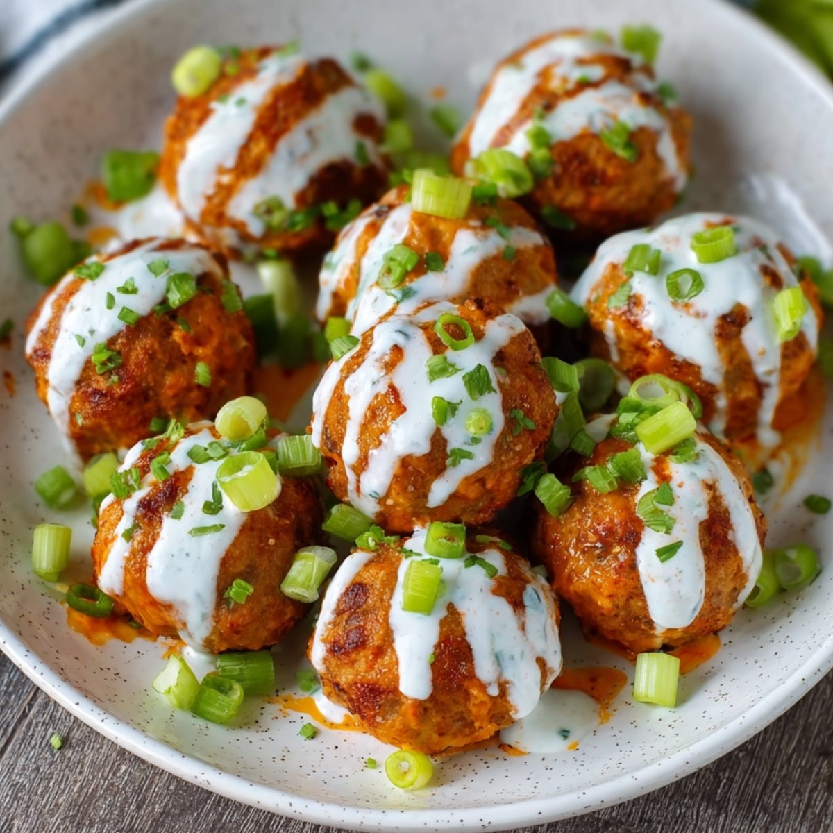 A close-up shot of cooked Buffalo Chicken Meatballs covered in spicy buffalo sauce, garnished with chopped green onions and served in a bowl.