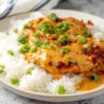 Chicken Diablo with creamy sauce, topped with chopped green onions, served over a bed of white rice.