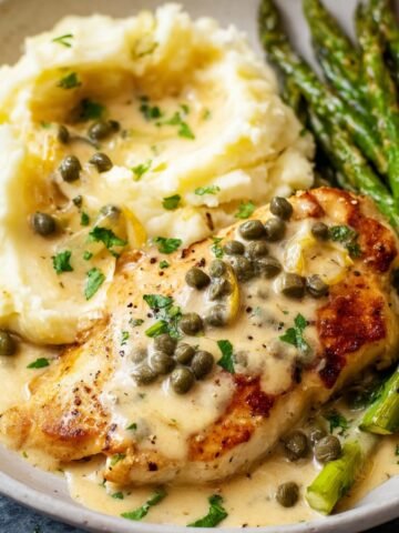 Chicken piccata served with mashed potatoes, capers, and asparagus.