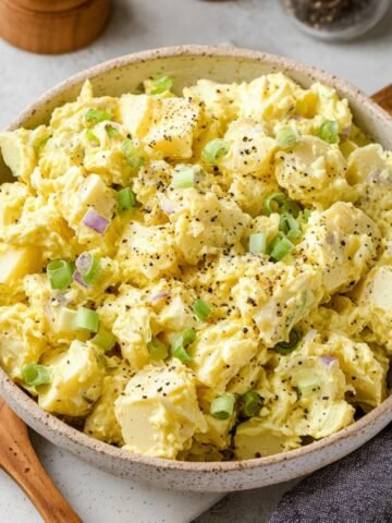 A creamy and freshly made classic potato salad, garnished with freshly ground black pepper and served in a light gray bowl.