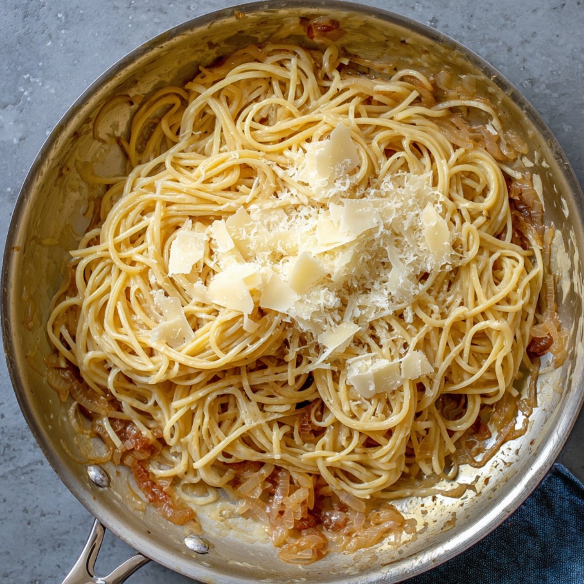A plate of spaghetti tossed with sweet, caramelized onions and garnished with herbs and parmesan.