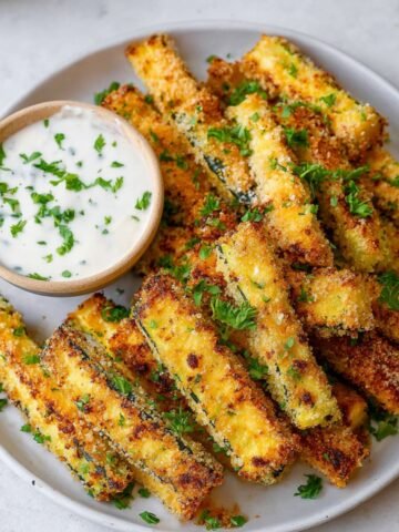 Crispy Baked Zucchini Fries garnished with parsley and served with a side of dipping sauce.