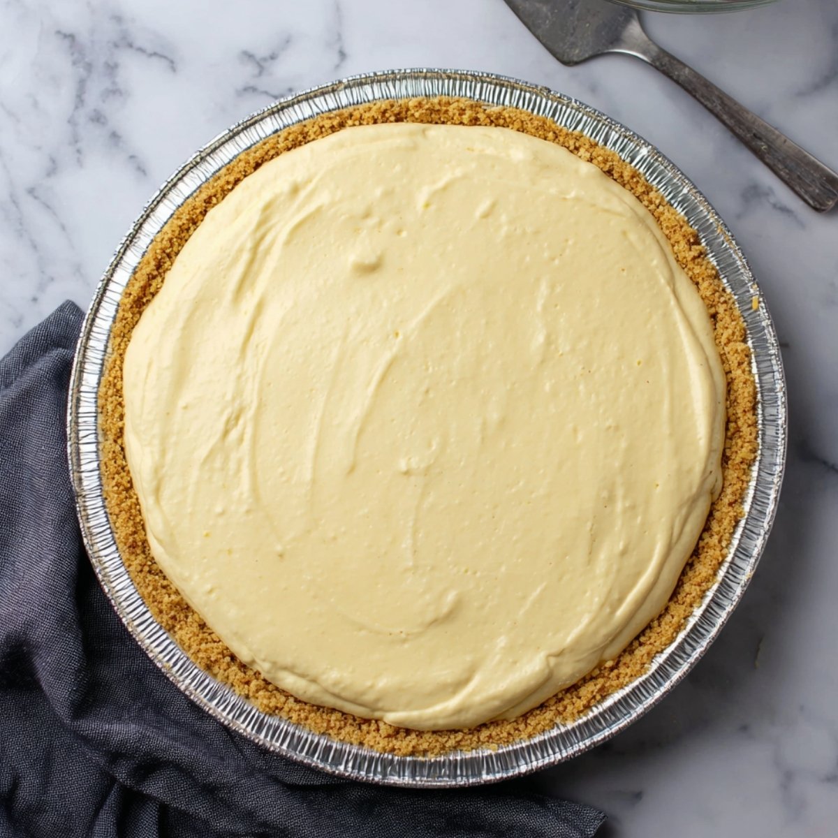 Whole no-bake eggnog pie in graham cracker crust before chilling on marble surface