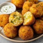 A close-up of Fried Rice Balls with a crispy breading and gooey cheese filling, served with dipping sauce.