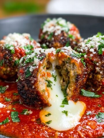 Homemade Mozzarella Stuffed Meatballs covered in marinara sauce, garnished with fresh parsley and grated cheese.