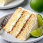 A slice of key lime cake on a plate, garnished with lime slices and frosting.