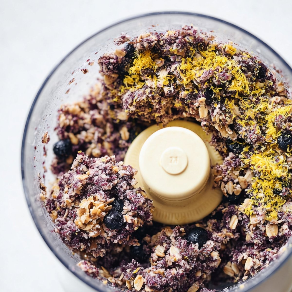 Blueberry energy ball mixture in a food processor with oats and fresh lemon zest added, before blending.