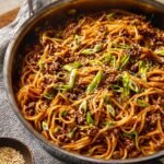 A skillet filled with Mongolian Ground Beef Noodles topped with green onions and sesame seeds, ready to be served.