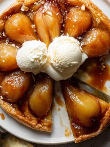 Pear Tarte Tatin Recipe with caramelized pears and flaky crust, topped with vanilla ice cream and one slice removed.