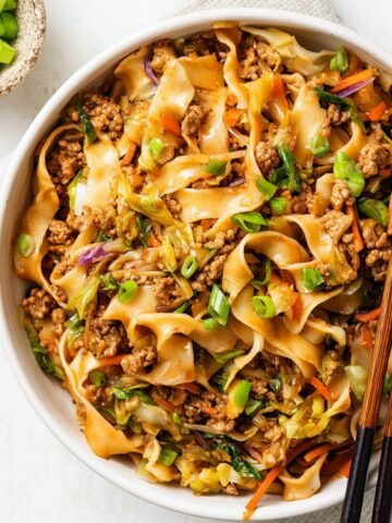 Potsticker Noodle Bowl with ground pork, cabbage, and wide noodles garnished with green onions and served with chopsticks
