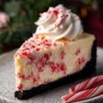 Close-up of a White Chocolate Peppermint Cheesecake slice with a whipped cream swirl and crushed peppermint on top.