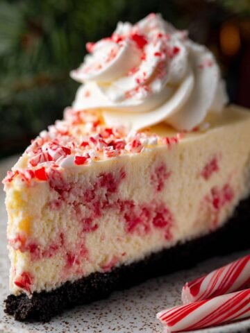 Close-up of a White Chocolate Peppermint Cheesecake slice with a whipped cream swirl and crushed peppermint on top.