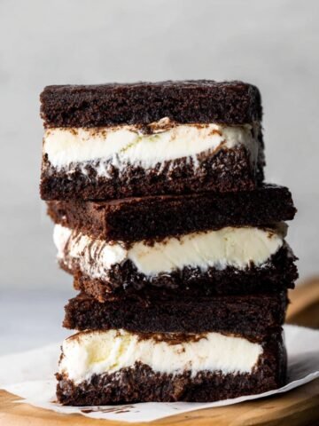 Brownie Ice Cream Sandwiches stacked on a white plate with layers of ice cream in between brownies.