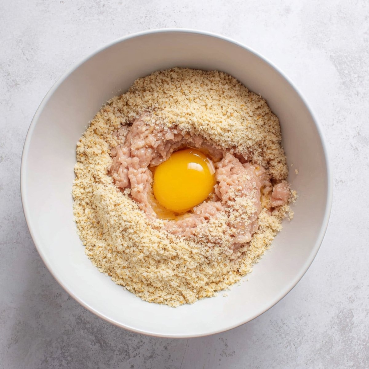 Ground chicken, breadcrumbs, and egg mixture in a white bowl