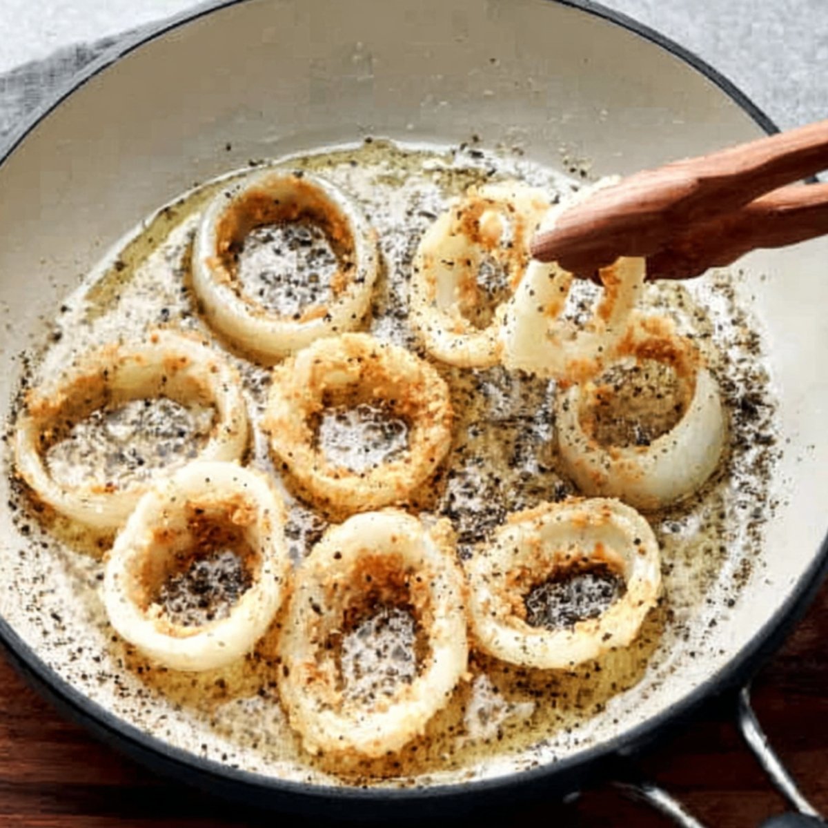Onion rings being cooked in a skillet with seasonings, lightly browned in oil.