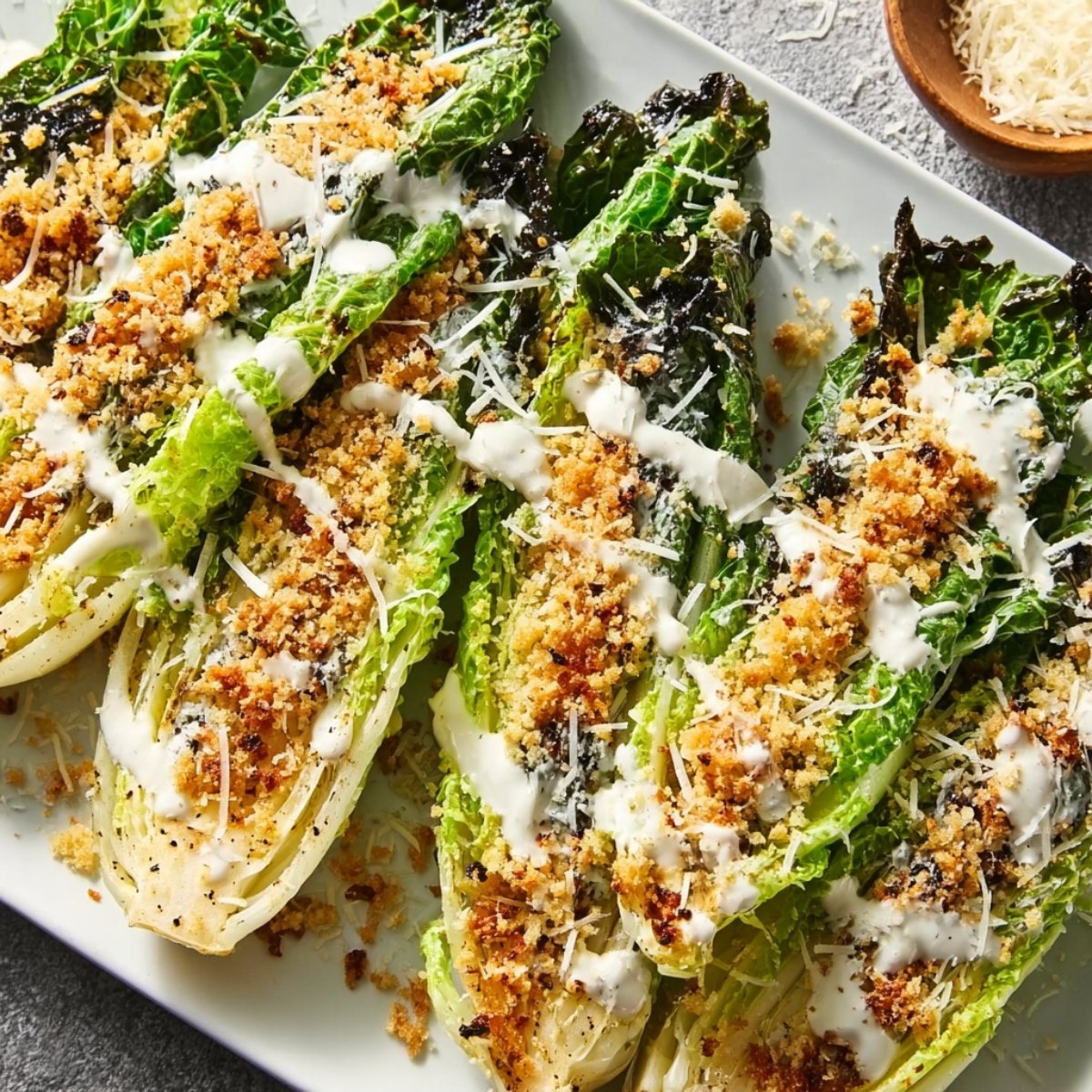 Grilled Romaine Caesar Salad lettuce topped with toasted panko breadcrumbs, grated parmesan, and Caesar dressing, offering a smoky and crunchy twist on the classic Caesar salad.