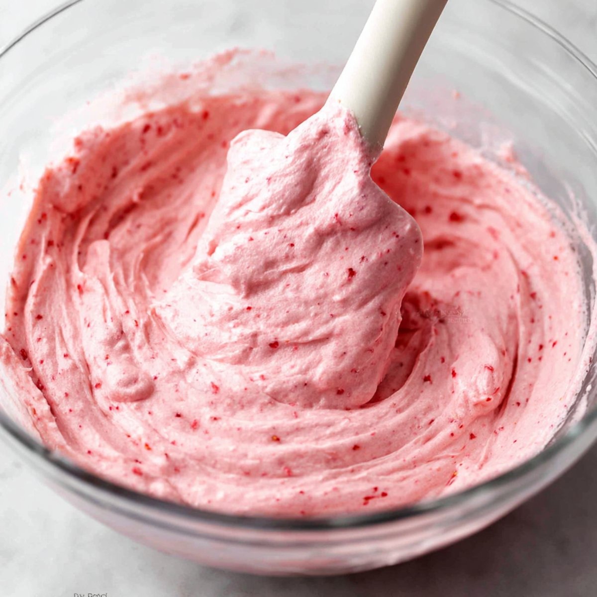 Pink strawberry buttercream frosting being mixed in a bowl.