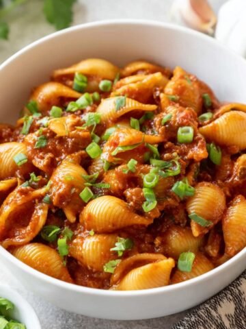 A close-up image of One Pot Beef Taco Pasta served in a bowl. The pasta shells are coated in a rich, savory tomato-based sauce, topped with fresh green onions, creating a hearty and flavorful meal.