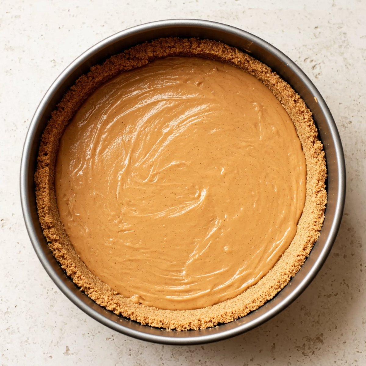 A springform pan with a smooth layer of caramel filling, perfectly spread over a graham cracker crust, ready to be chilled for a Banoffee pie.