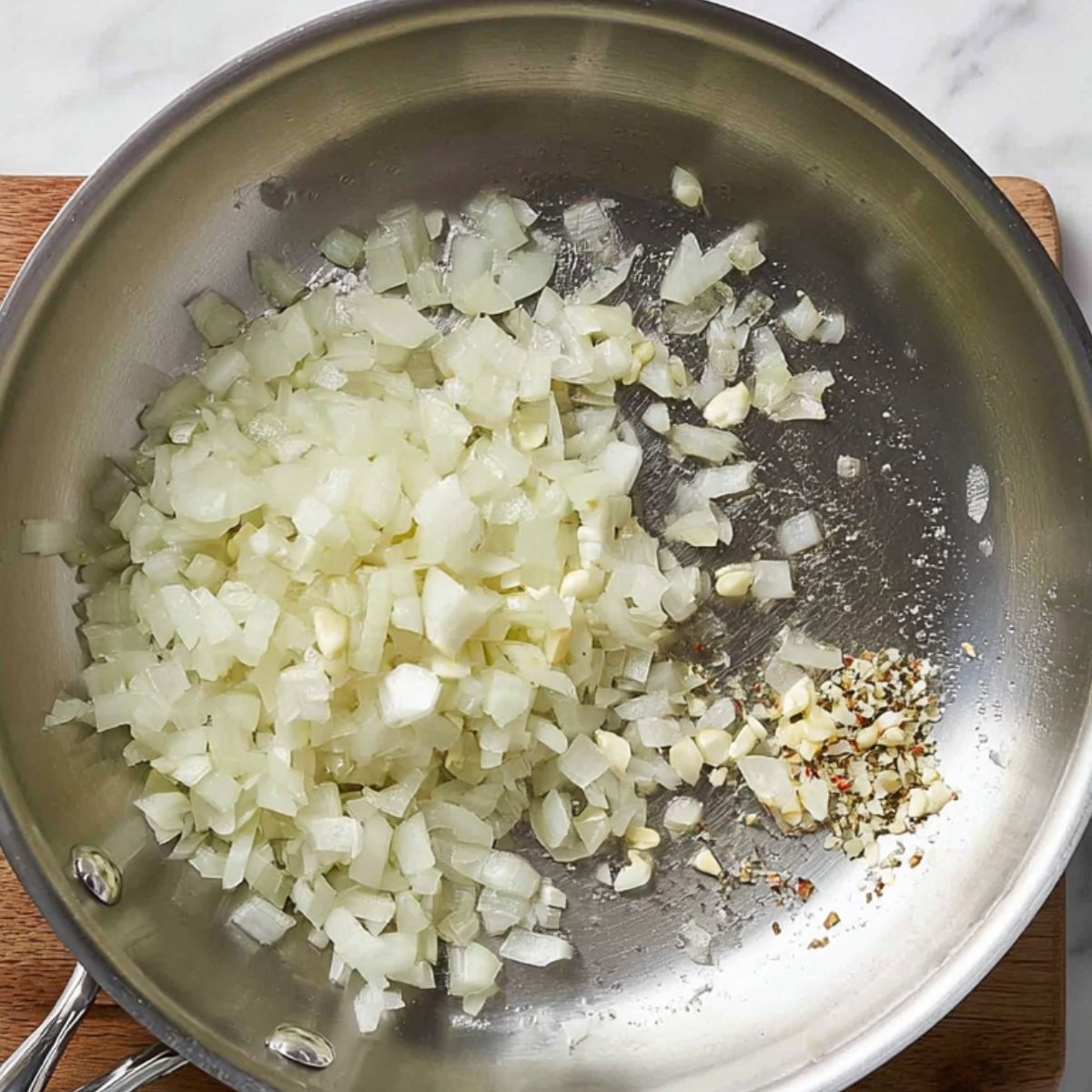Sautéed onions and garlic in a pan, with seasonings and oil, creating a fragrant base for a dish.