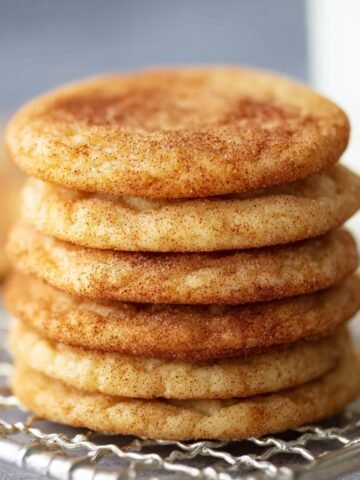 Freshly baked Snickerdoodle Cookies stacked on a wire rack with a glass of milk.