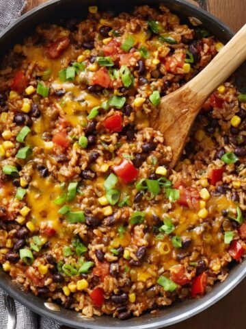 A hearty Southwest Lentils and Rice Skillet with melted cheese, black beans, corn, and diced tomatoes, topped with fresh green onions for garnish.