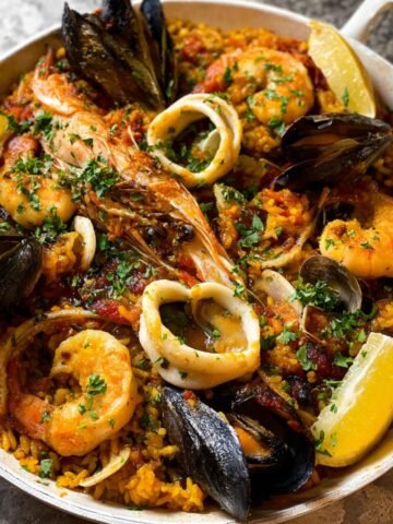 A vibrant Spanish Paella with shrimp, squid, and mussels garnished with parsley and lemon wedges, showcasing Spanish flavors.