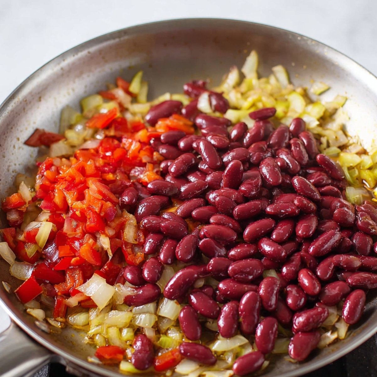 Kidney beans being added into a skillet containing sautéed vegetables like onions and peppers for a quesadilla filling.