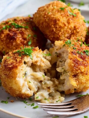 Golden-brown Chicken Croquettes with a crispy crust, some cut open to reveal the creamy filling inside, garnished with parsley.
