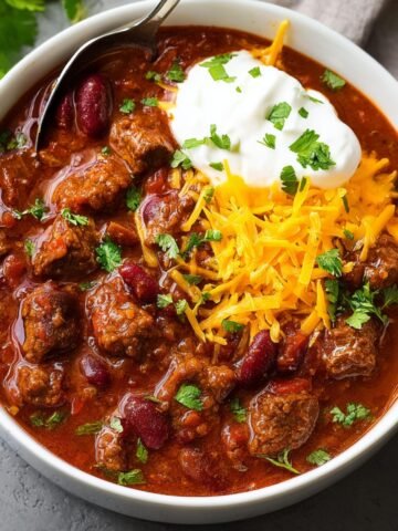 A hearty bowl of Chili Con Carne topped with shredded cheese, sour cream, and fresh cilantro.