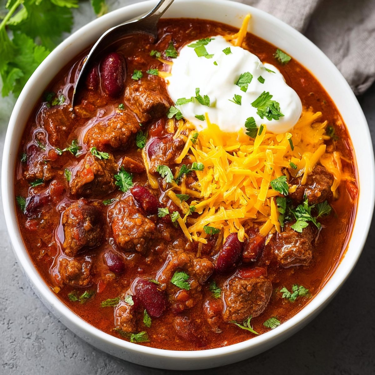 A hearty bowl of Chili Con Carne topped with shredded cheese, sour cream, and fresh cilantro.