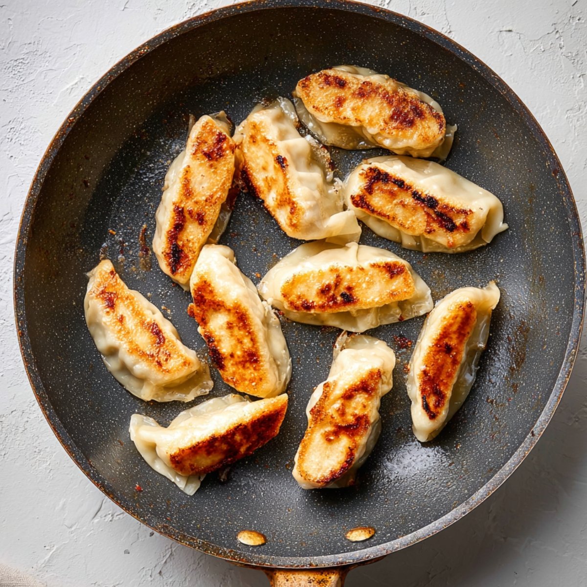 A frying pan with golden-brown dumplings, showcasing their crispy sear on one side, cooking on a stovetop.