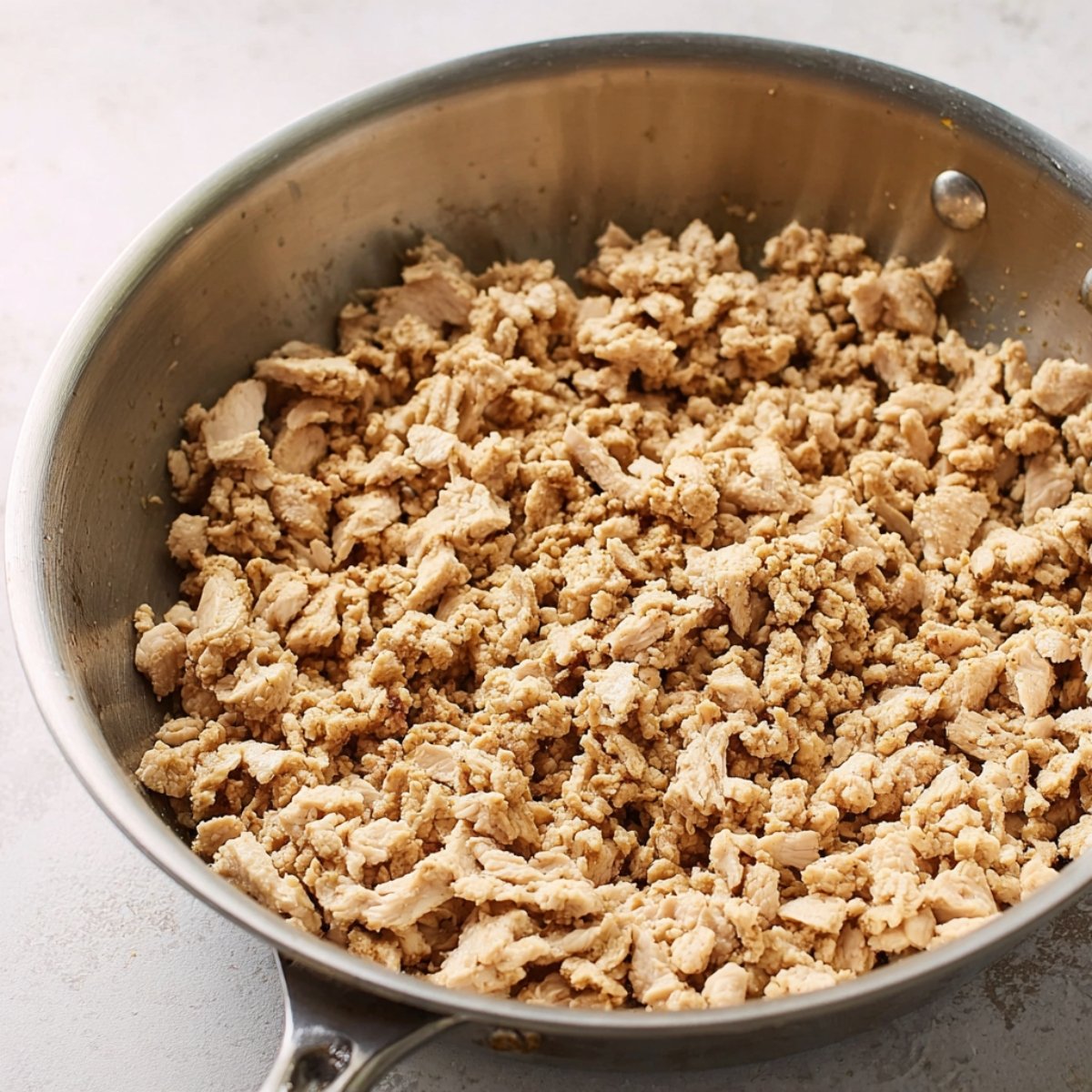 Ground chicken cooking in a skillet, breaking down into smaller pieces as it is sautéed.