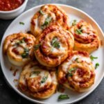 A plate of golden, baked Homemade Pepperoni Pizza Rolls, with melted cheese, marinara sauce, and fresh basil, perfect for serving as a snack or appetizer.
