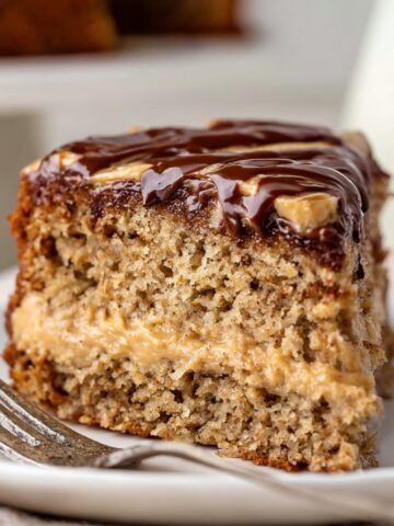 A slice of peanut butter banana cake with a layer of peanut butter filling, topped with a glossy layer of chocolate ganache, showcasing the moist texture of the cake and the rich filling.