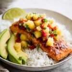 A plate of Pineapple Salsa Salmon fillets topped with vibrant pineapple salsa, served with avocado slices and white rice, garnished with fresh cilantro.