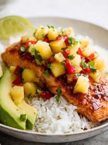 A plate of Pineapple Salsa Salmon fillets topped with vibrant pineapple salsa, served with avocado slices and white rice, garnished with fresh cilantro.