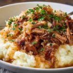 Tender pulled Pork and Sauerkraut served over creamy mashed potatoes, garnished with fresh parsley.
