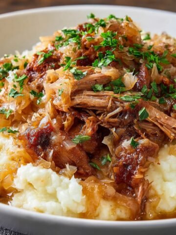 Tender pulled Pork and Sauerkraut served over creamy mashed potatoes, garnished with fresh parsley.