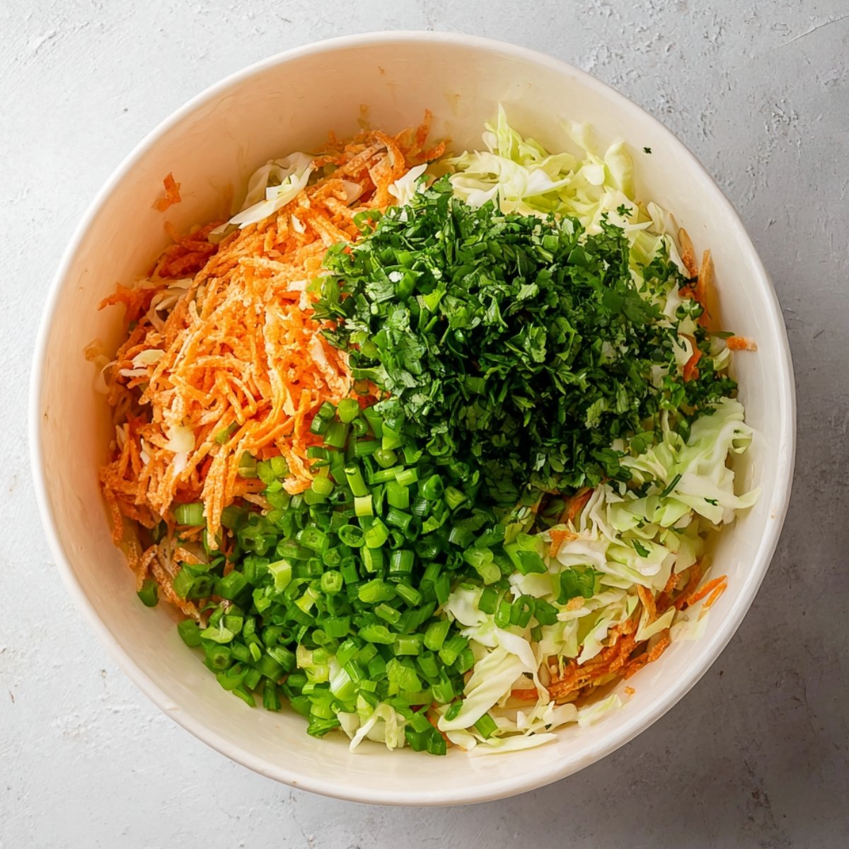 A bowl filled with shredded cabbage, grated carrots, chopped green onions, and fresh cilantro, ready to be mixed for a vibrant salad.