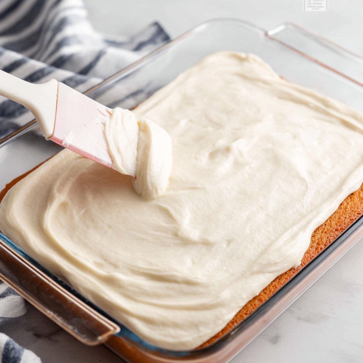 Cream cheese layer being spread on cake.